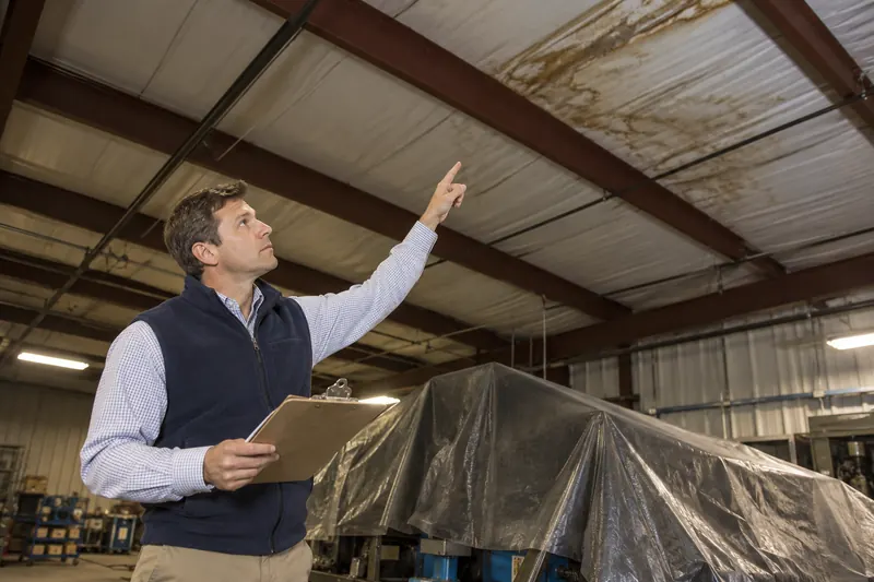 Facility manager pointing to a stained metal roof deck inside a plant